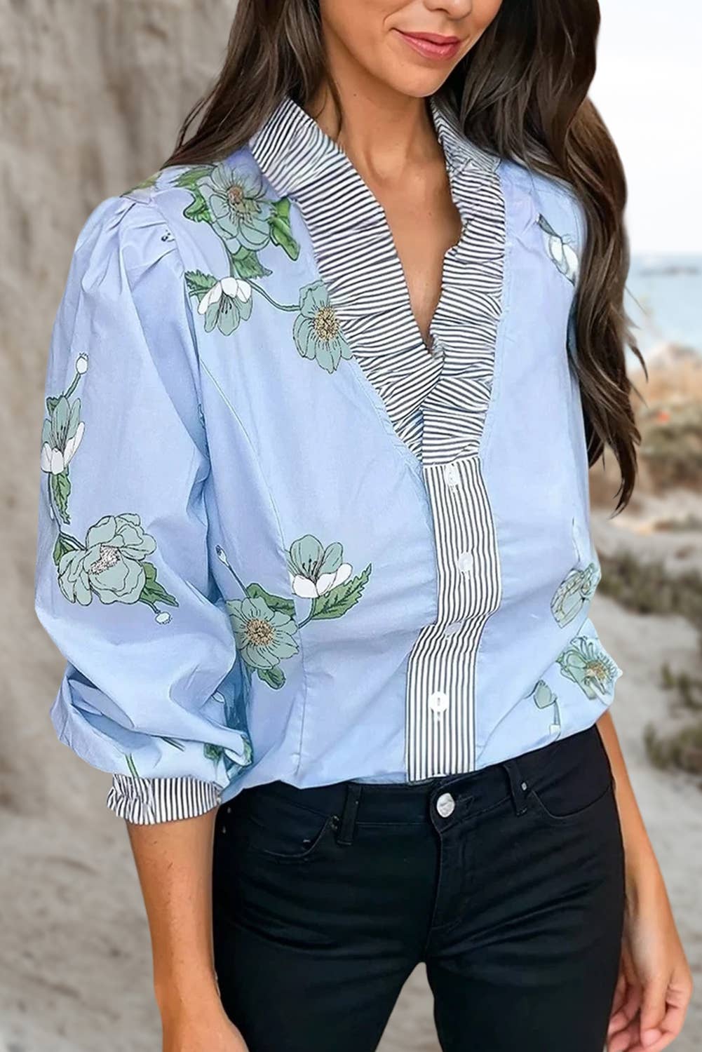 Woman wearing a light blue floral blouse with a striped collar at the beach.