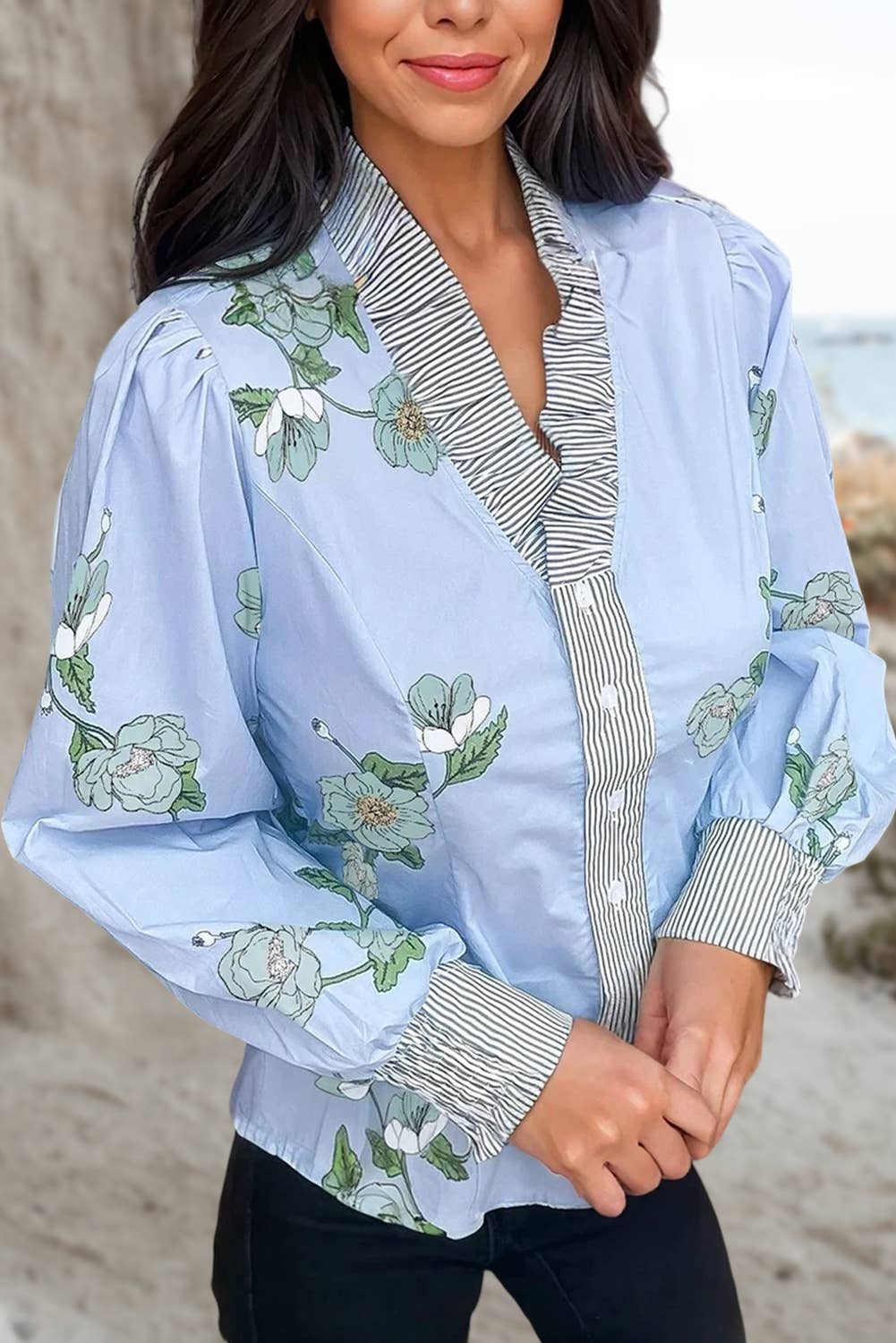Light blue floral blouse with striped sleeves worn by a  woman untucked with black jeans